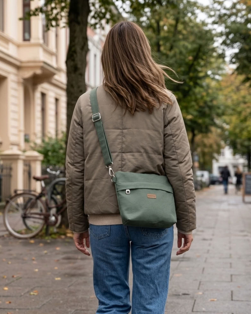 GRETJE Umhängetasche in Pine Green, getragen über einer olivfarbenen Jacke bei einem herbstlichen Stadtspaziergang.